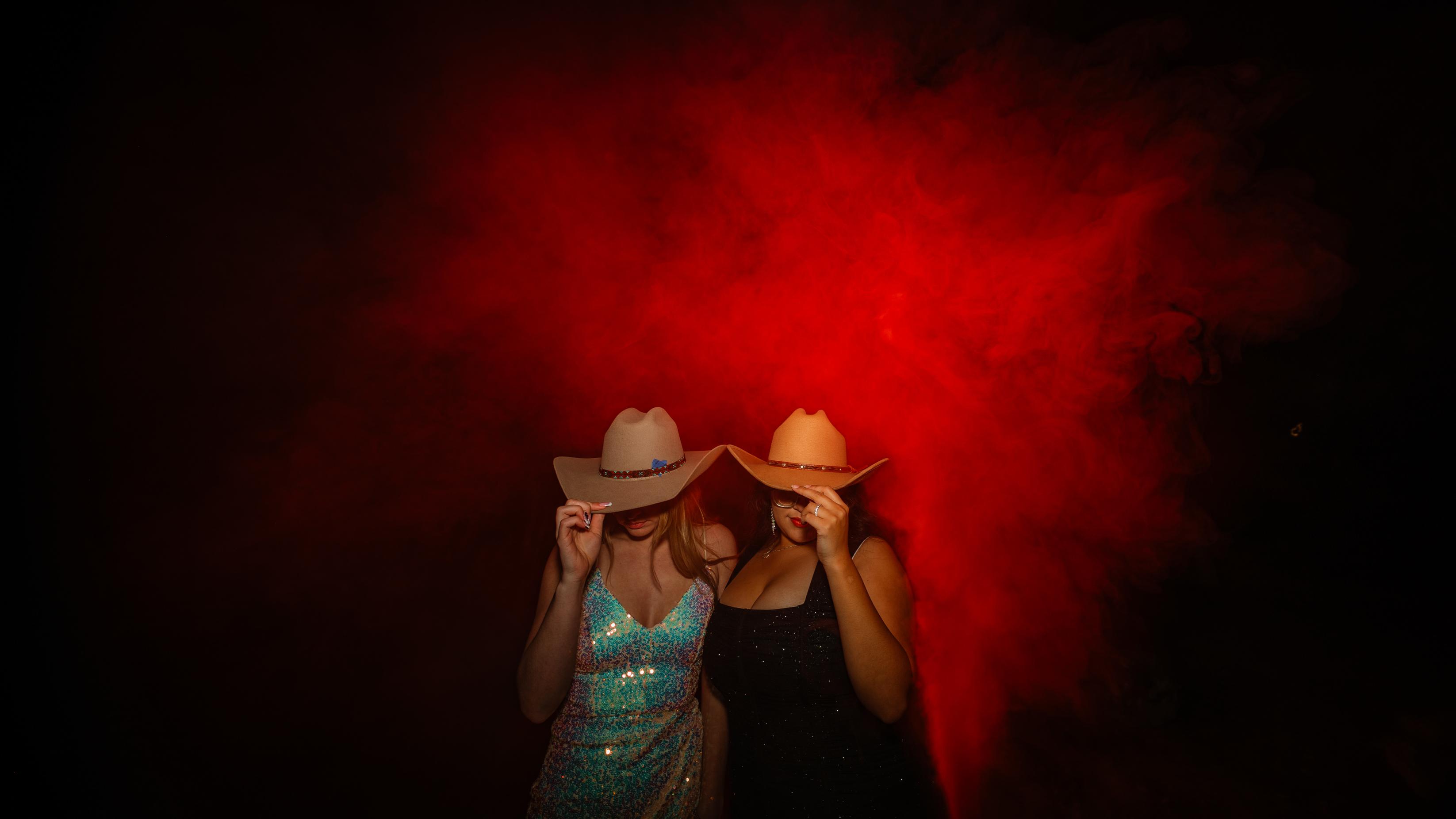 Two women emerging from red smoke tipping their cowboy hats