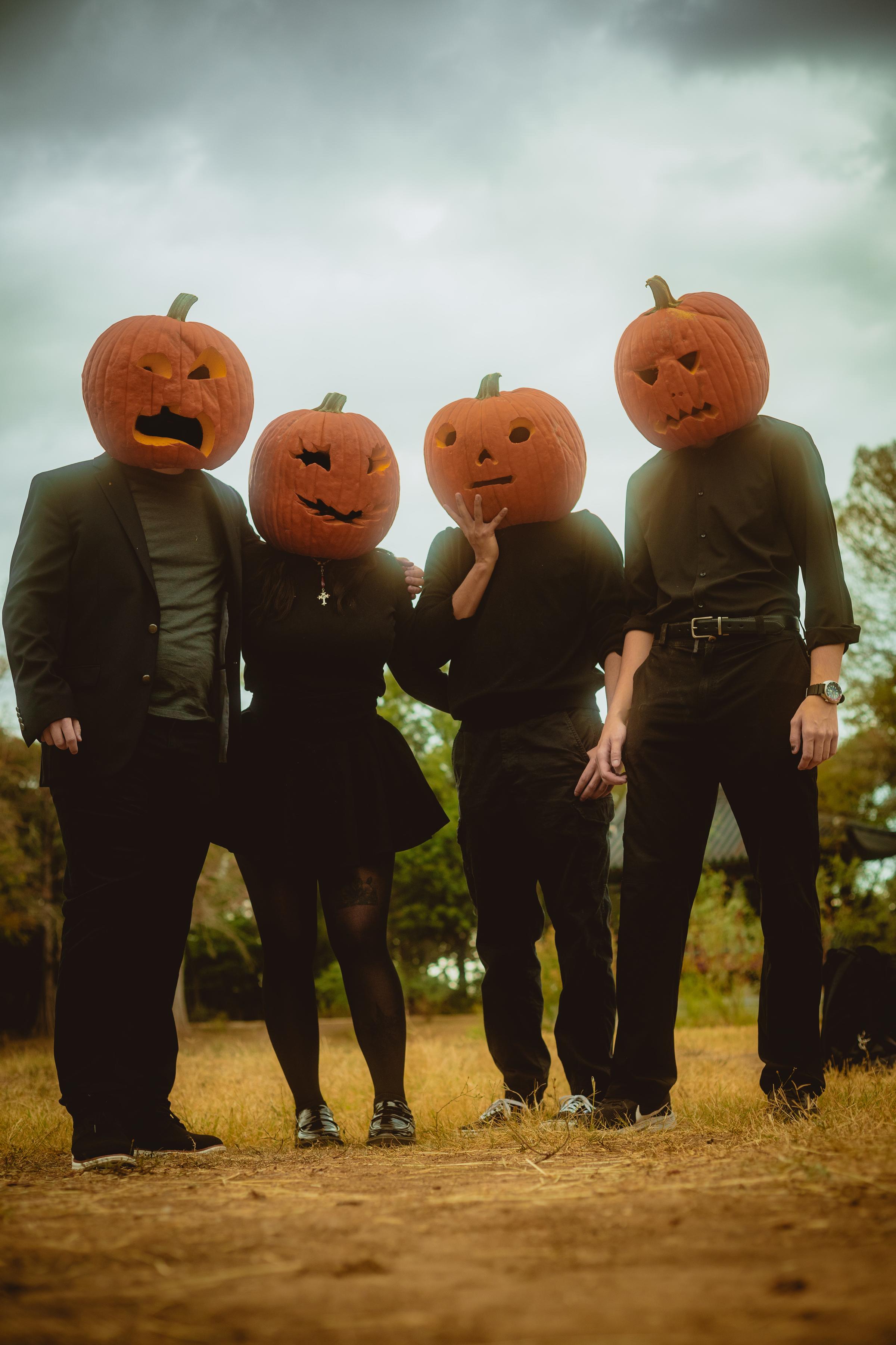 Four people with pumpkins on their heads, dressed in black standing side by side.